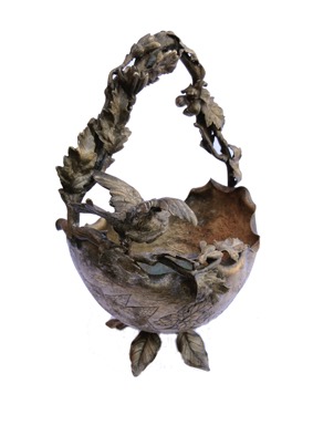 Metal basket with intertwined branches for handle. Bird ready to fly, perched on the wing. Upside down structure of a helmet.