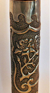 Shell with medallion filled with roses. Top and bottom have a wavy pattern. Back embossed.