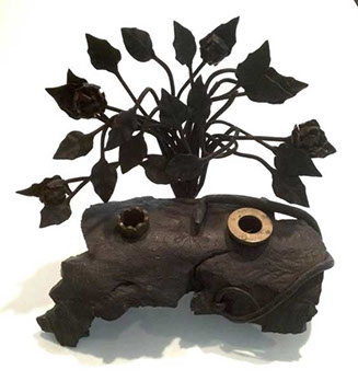 Piece of ordnance debris, transformed into an inkwell, engraved Ricordo de M. Cimone,1917,&nbsp; with a vertical bouquet of leaves as background.