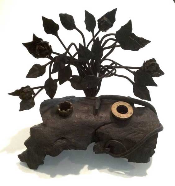 Piece of ordnance debris, transformed into an inkwell, engraved Ricordo de M. Cimone,1917,&nbsp; with a vertical bouquet of leaves as background.
